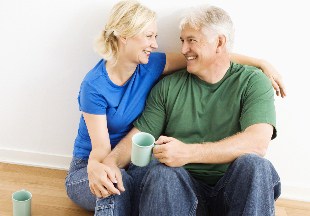 Middle-aged couple sitting on floor snuggling and drinking coffee.
