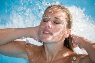 Beautiful blond woman under a small waterfall in the swimmingpool (shallow dof)